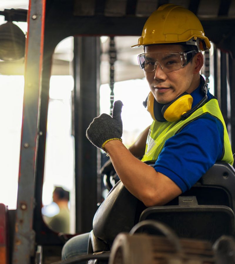 Engineer or technician Concept. A male employee driving a forklift and showing thumb up in factory.